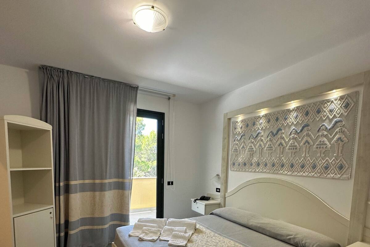 Une chambre à coucher comprenant un lit, une table de chevet, une armoire, un tapis à motifs et une vue sur l’extérieur par une fenêtre.