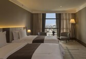 A hotel room with two beds, a chair, a TV, and a view of the city.