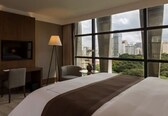 A hotel room with a large bed, a desk, a chair, a TV mounted on the wall, and a window with a city view.
