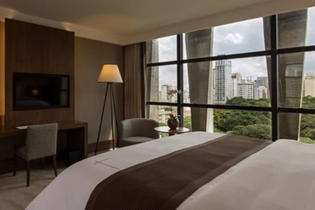 Habitación de hotel con una cama grande, un escritorio, una silla, un televisor montado en la pared y una ventana con vista a la ciudad.