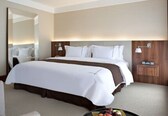 A hotel room with a large bed, a bedside table, a mirror, and a wall-mounted lamp.