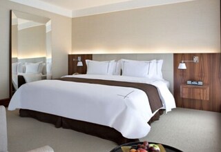 A hotel room with a large bed, a bedside table, a mirror, and a wall-mounted lamp.