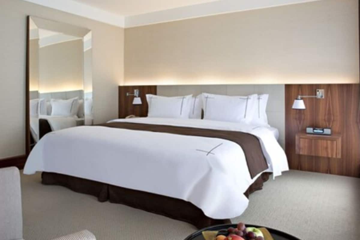 A hotel room with a large bed, a bedside table, a mirror, and a wall-mounted lamp.