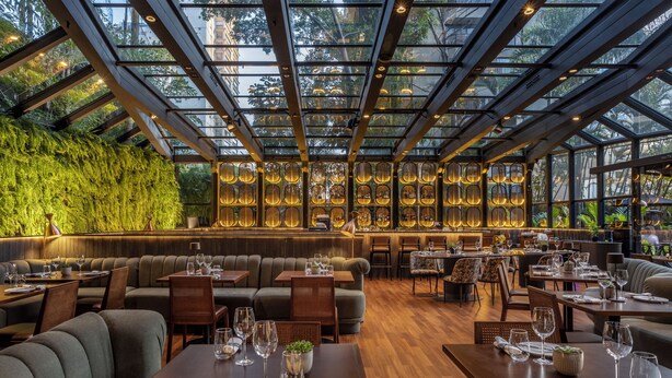Un restaurante con techo de vidrio, pared verde y varias mesas de comedor dispuestas con copas de vino y platos.