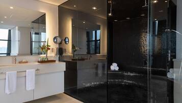 Un baño moderno con ducha de vidrio, un espejo grande y tocador con lavamanos y perchero.