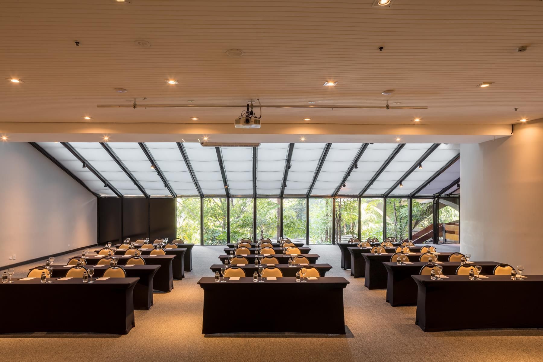 Une salle de conférence dotée de plusieurs tables et chaises, de grandes fenêtres et d’un plafond haut avec des poutres apparentes.