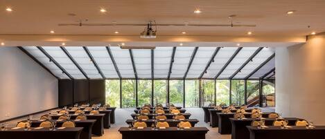 Un salón de conferencias con varias mesas y sillas, ventanas amplias y un techo alto con vigas a la vista.
