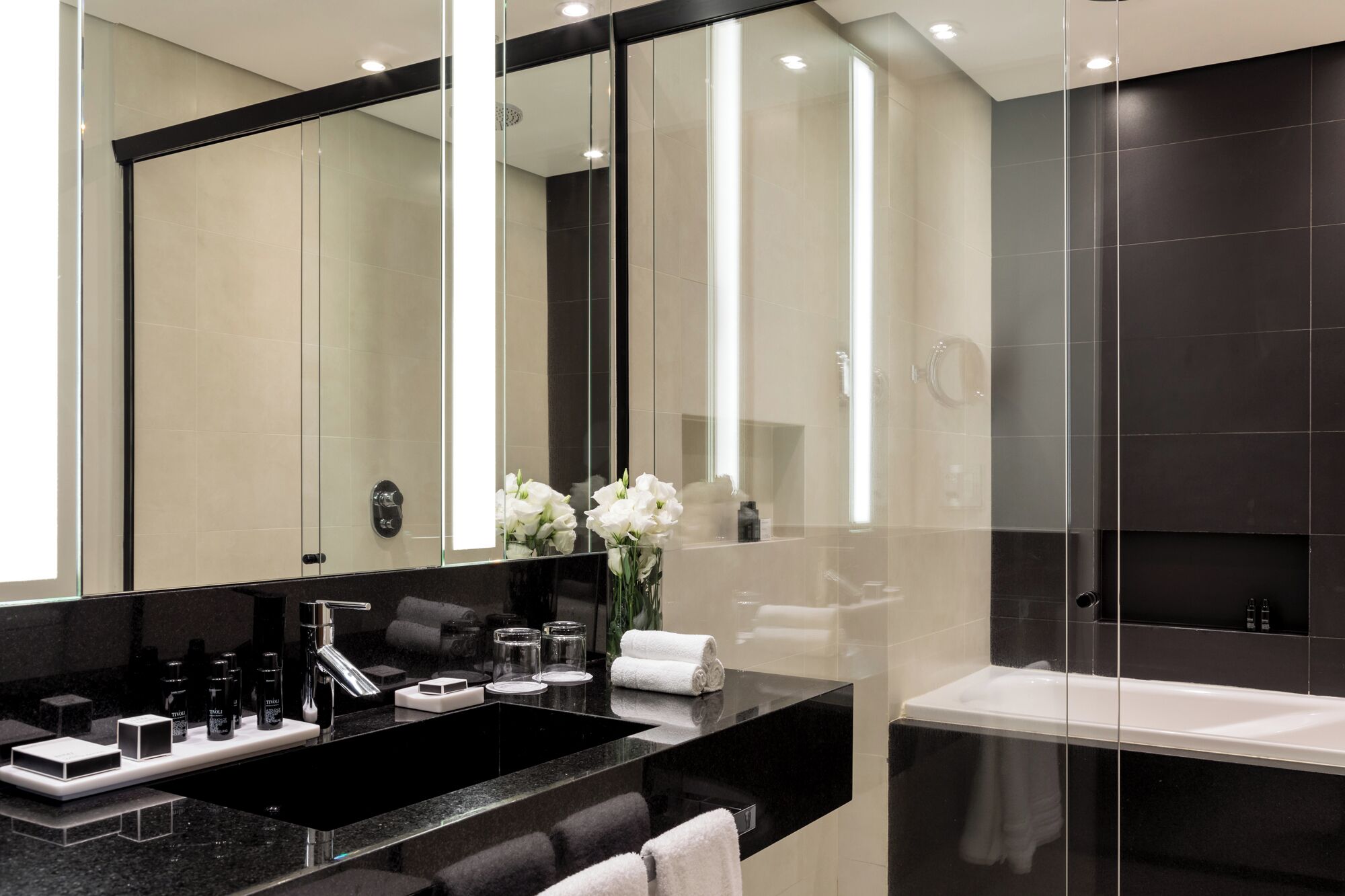 Un bagno moderno con un piano lavabo nero, uno specchio grande e una vasca da bagno bianca.
