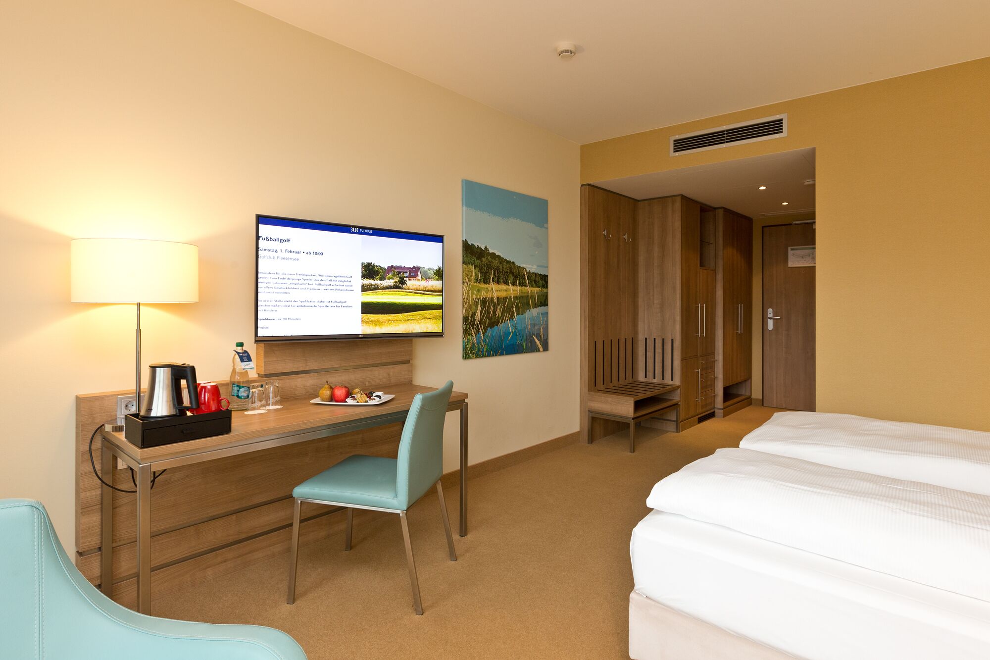 A hotel room with a desk, chair, bed, and a TV displaying a webpage.