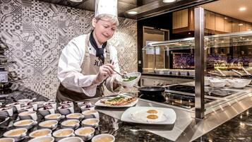 A chef preparing food in a modern kitchen with patterned tiles, stainless steel appliances, and a display case of dishes.