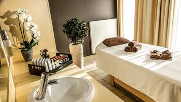 A hotel room with a bed, a sink, a mirror, toiletries, and a potted plant.