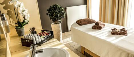 A hotel room with a bed, a sink, a mirror, toiletries, and a potted plant.