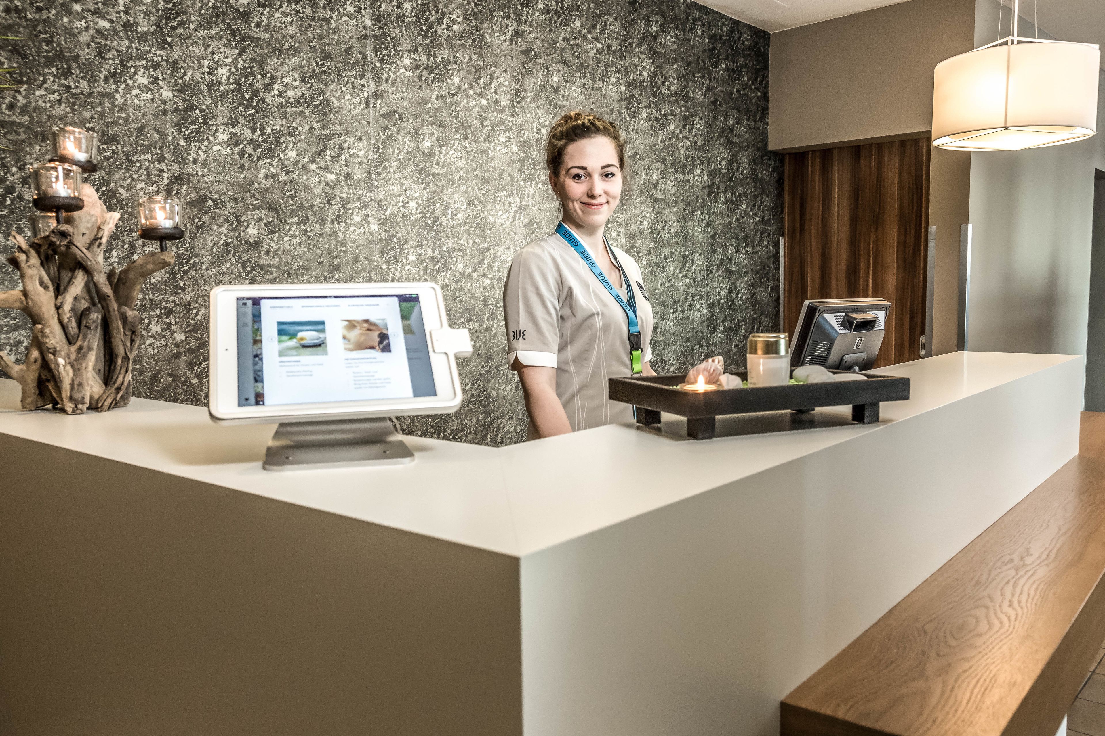En receptionsdisk med en datorskärm, en kassa och en dekorativ trädetalj.