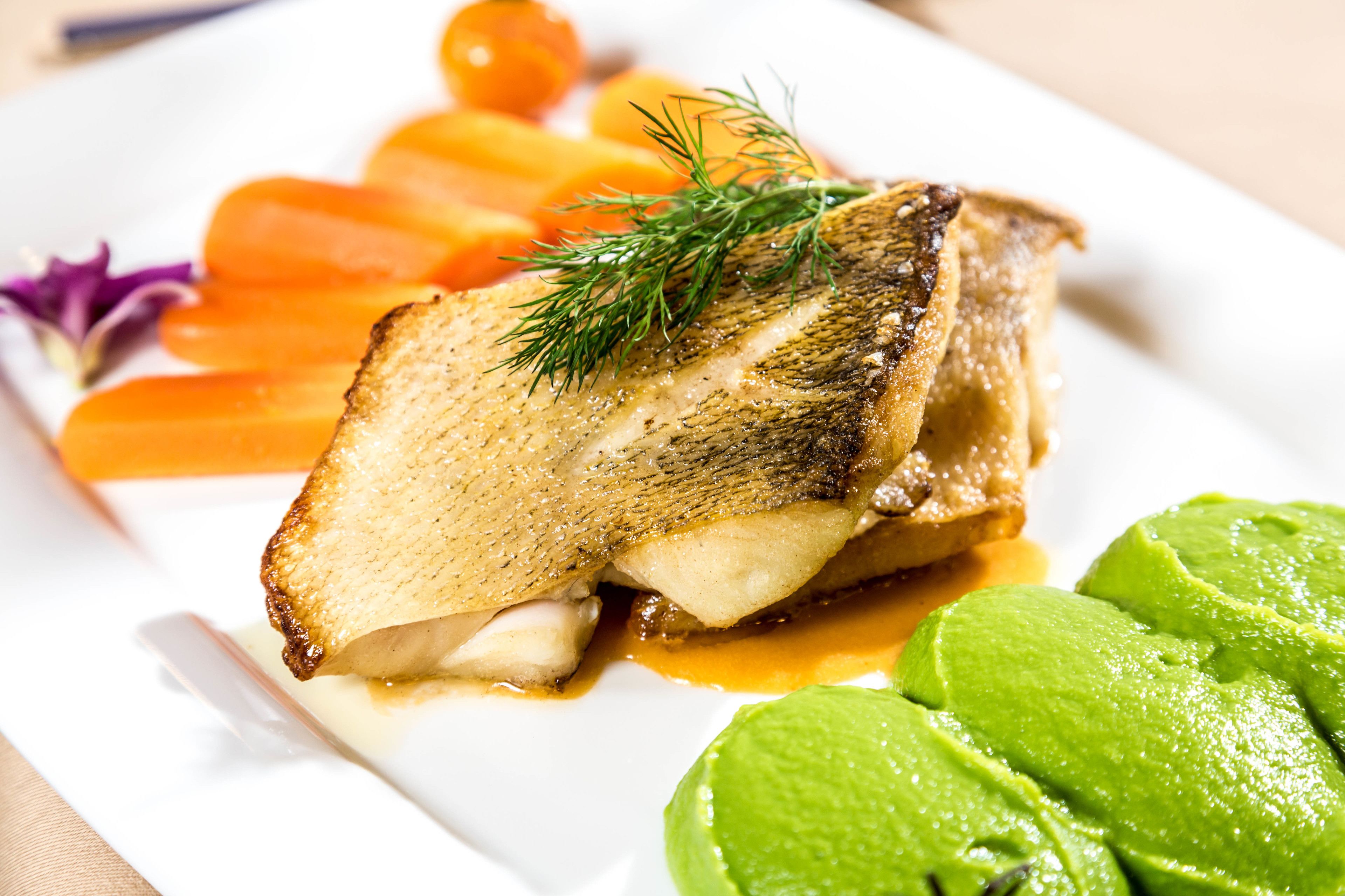 Un plato con pescado, zanahorias y una guarnición verde.