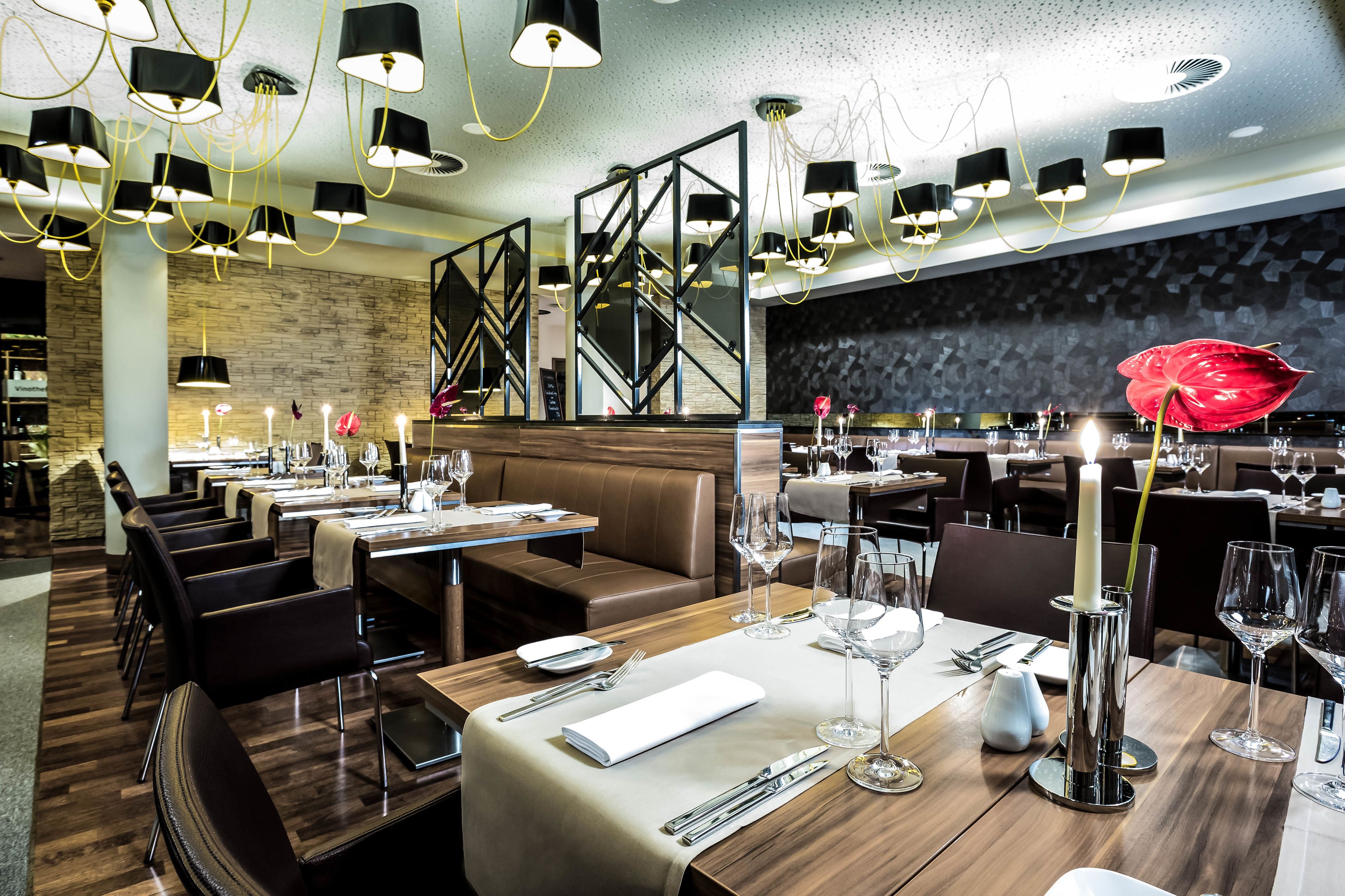 Um restaurante moderno com várias mesas, cadeiras pretas e luminárias contemporâneas.