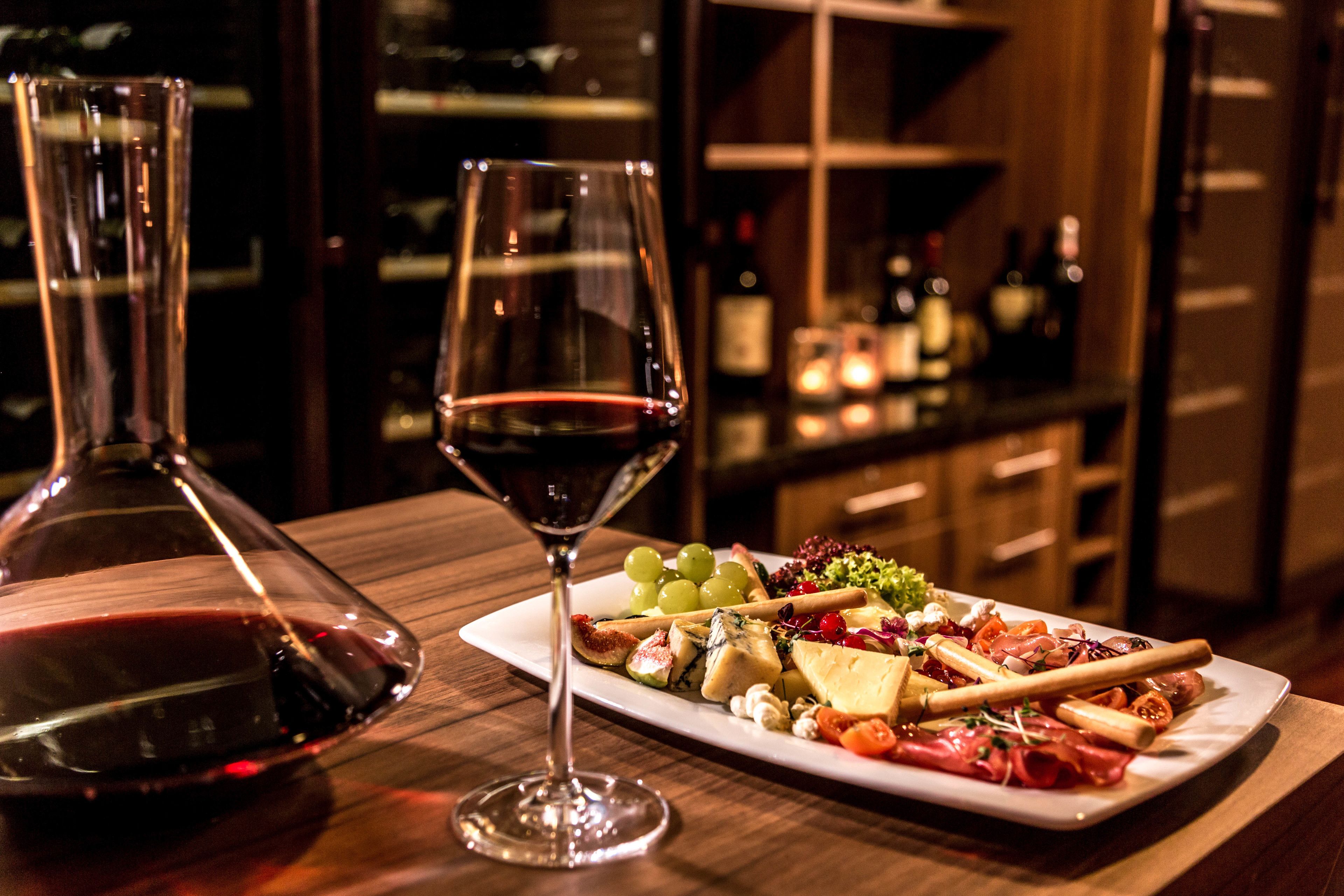 A charcuterie board with various cheeses, meats, and fruits, accompanied by two glasses of red wine on a wooden table.