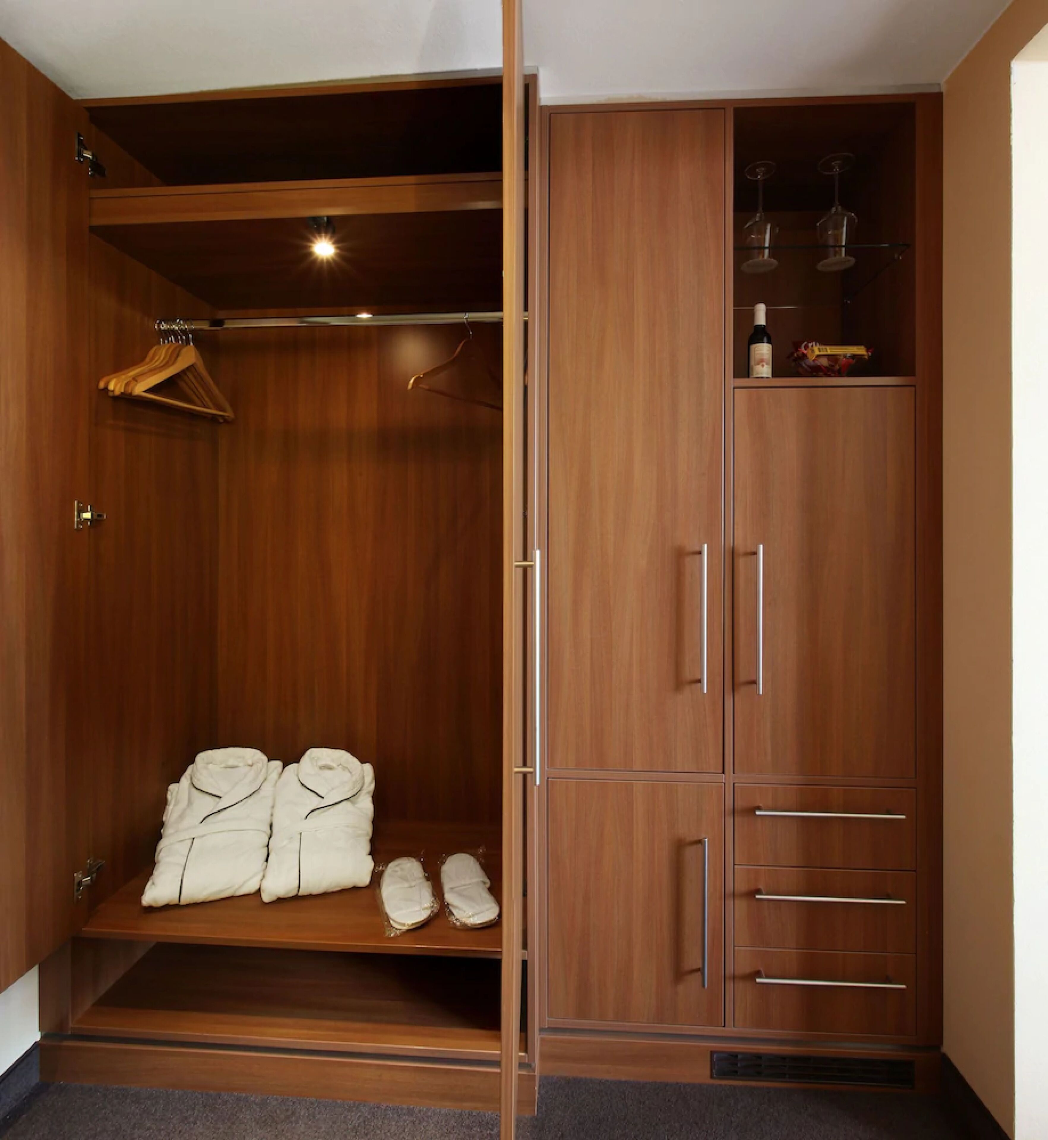 Un vestidor con puertas de madera, una barra para colgar ropa y un estante con copas de vino.