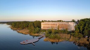 Un grand hôtel à étages, avec une jetée s’avançant dans une étendue d’eau calme, le tout entouré d’une végétation luxuriante.
