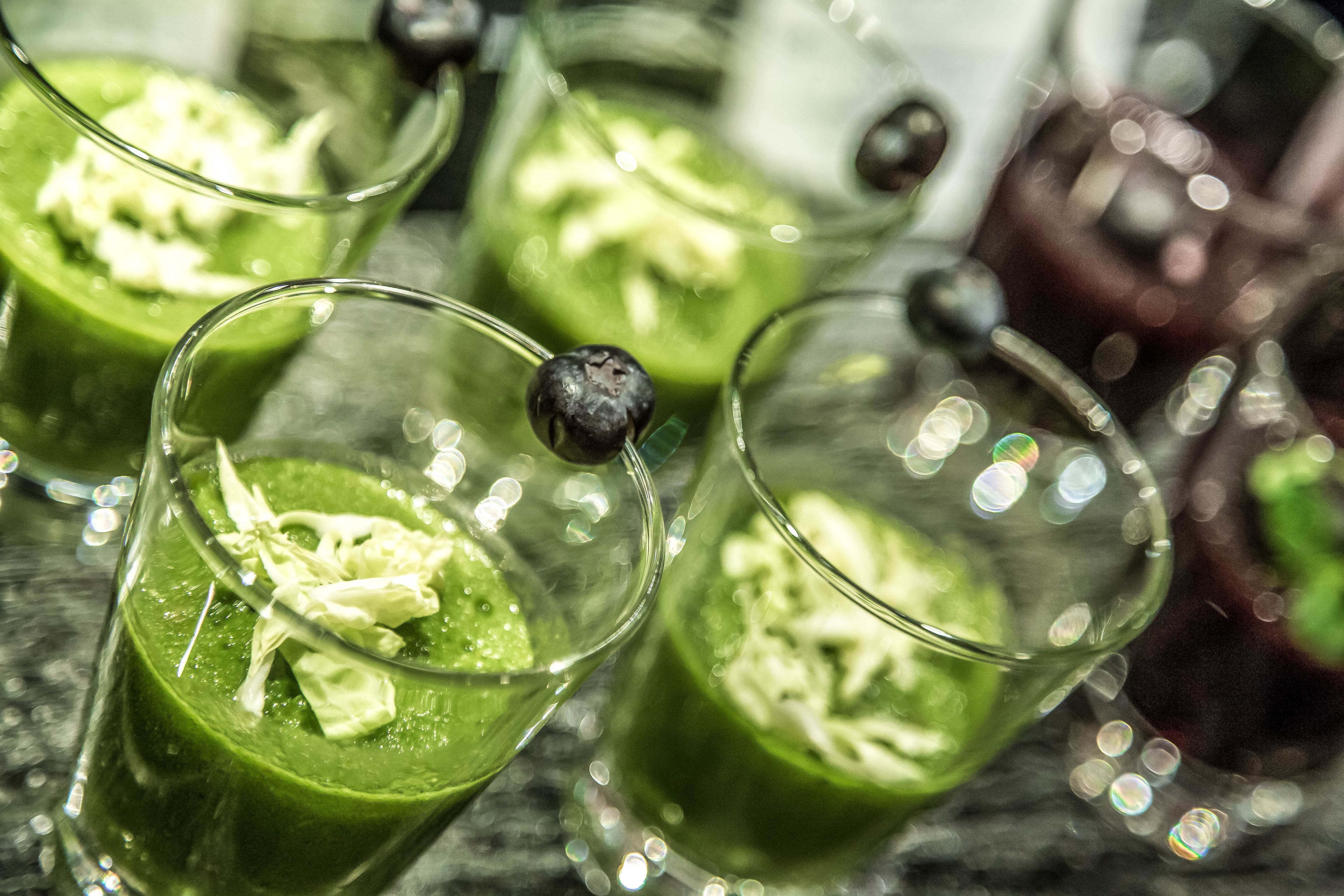 A close-up of a green beverage in a glass with a blueberry garnish.