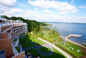 A hotel with multiple balconies overlooking a lake, a well-maintained lawn, and a dock extending into the water.