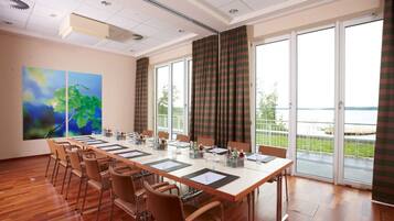 Un salón de conferencias con una larga mesa, sillas y ventanas grandes con cortinas.