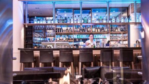 Un espace bar avec un barman, des étagères remplies de bouteilles d’alcool et des sièges disposés autour d’un foyer.