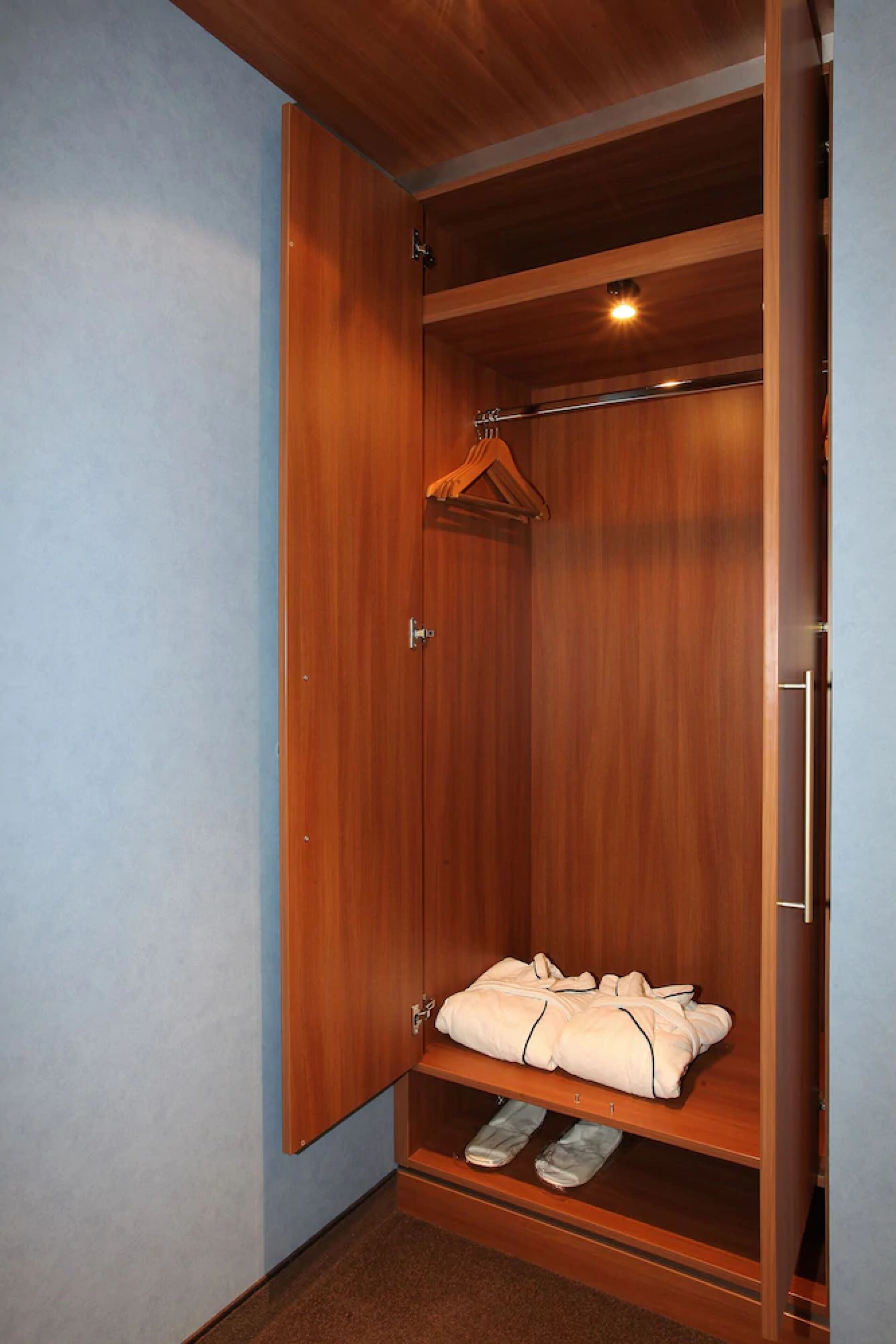 A wooden wardrobe with a hanging rod and a shelf for folded clothes.