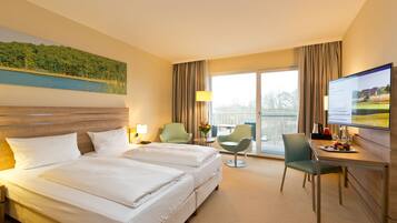 A hotel room with a bed, two chairs, a desk, a TV, and a window with curtains.