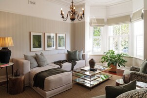 Een goed verlichte woonkamer met een bank, bijzettafeltje en een groot raam met zonwering.