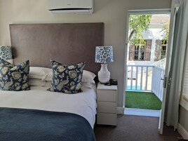 A bedroom with a bed, two decorative pillows, a bedside lamp, a nightstand, and a view of a balcony with a pool.