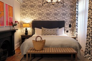 A bedroom with a bed, bedside tables, a lamp, a fireplace, and a patterned wallpaper.