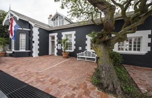 A black and white building with a flag, a bench, and a tree.