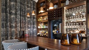 Uma área de bar com cadeiras listradas, balcão de madeira e prateleiras com garrafas e copos.