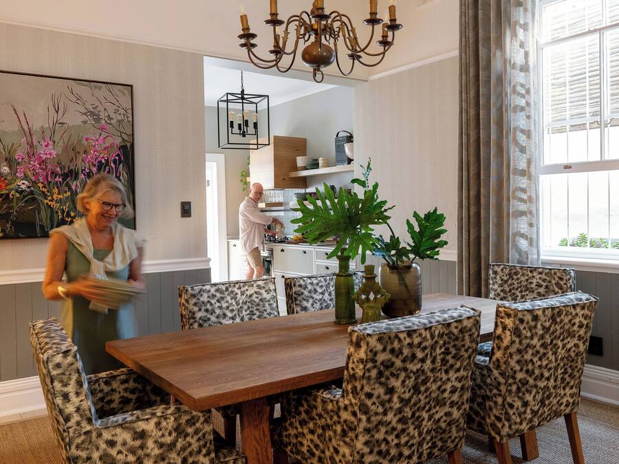 A dining area with a wooden table and leopard print chairs, a chandelier, and a large floral painting on the wall.