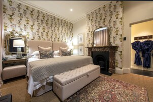 A bedroom with a large bed, a bench, a fireplace, and a robe rack.