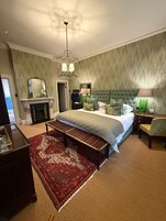 A bedroom with a bed, a bench, a fireplace, a mirror, a lamp, and a patterned carpet.