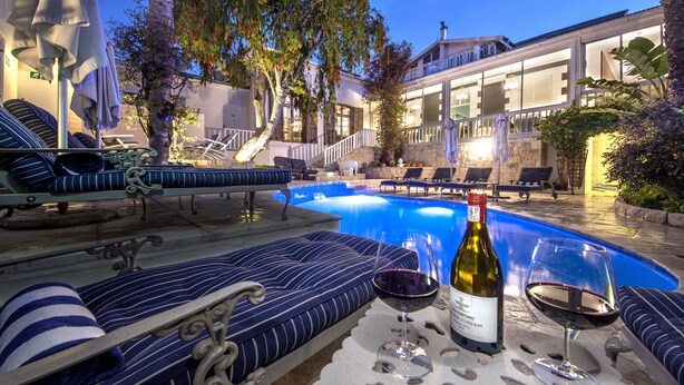 Área junto à piscina com espreguiçadeiras, uma garrafa de vinho e copos sobre uma mesa.