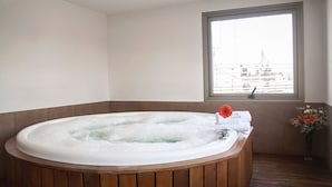 Un jacuzzi en una habitación con un ventanal grande, suelo de madera y un jarrón con flores.