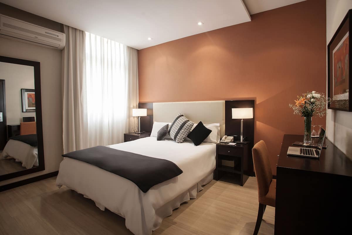 Hotellihuone, jossa on suuri sänky, yöpöydät, työpöytä ja tuoli.