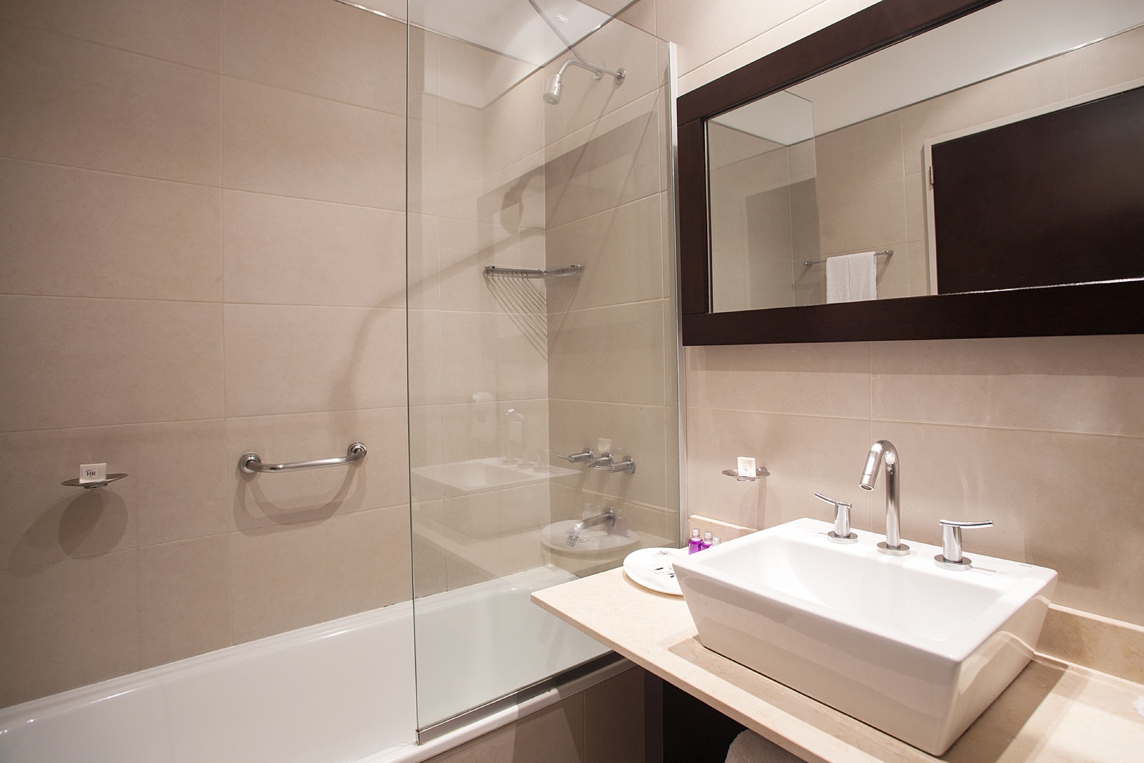 A modern bathroom with a glass-enclosed shower, a bathtub, and a vanity with a sink and mirror.