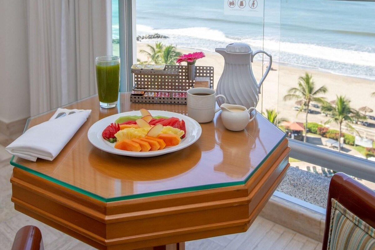 Un balcon avec une table préparée pour le petit-déjeuner, une vue sur la plage et un ciel dégagé.