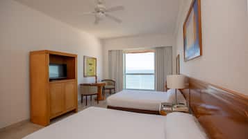 A hotel room with two beds, a TV, a desk with a chair, a ceiling fan, and a window with curtains.