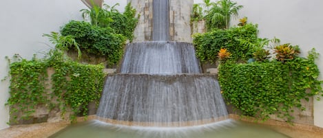Una cascada de varios niveles en un patio con abundante vegetación y una piscina en la base.