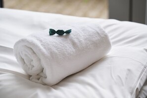 A neatly rolled white towel on a bed with a green bow.