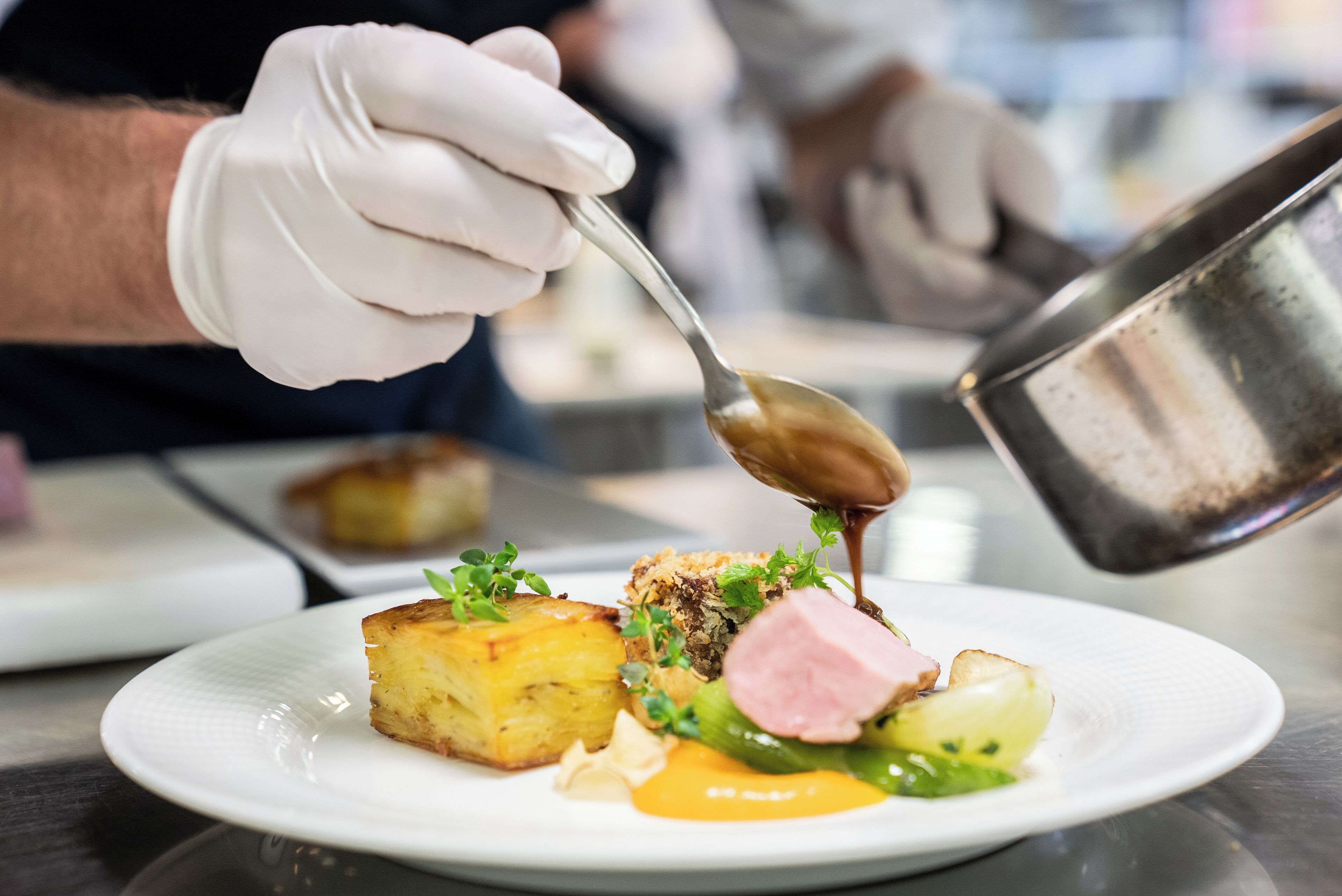 A chef pouring sauce onto a plated dish.