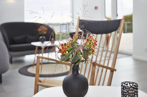 Un salon moderne avec une table ronde, un vase foncé orné de baies rouges et une chaise en bois.