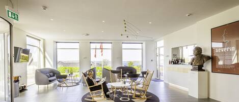 A modern lobby with a circular seating area, large windows, and a reception desk with a bust sculpture.