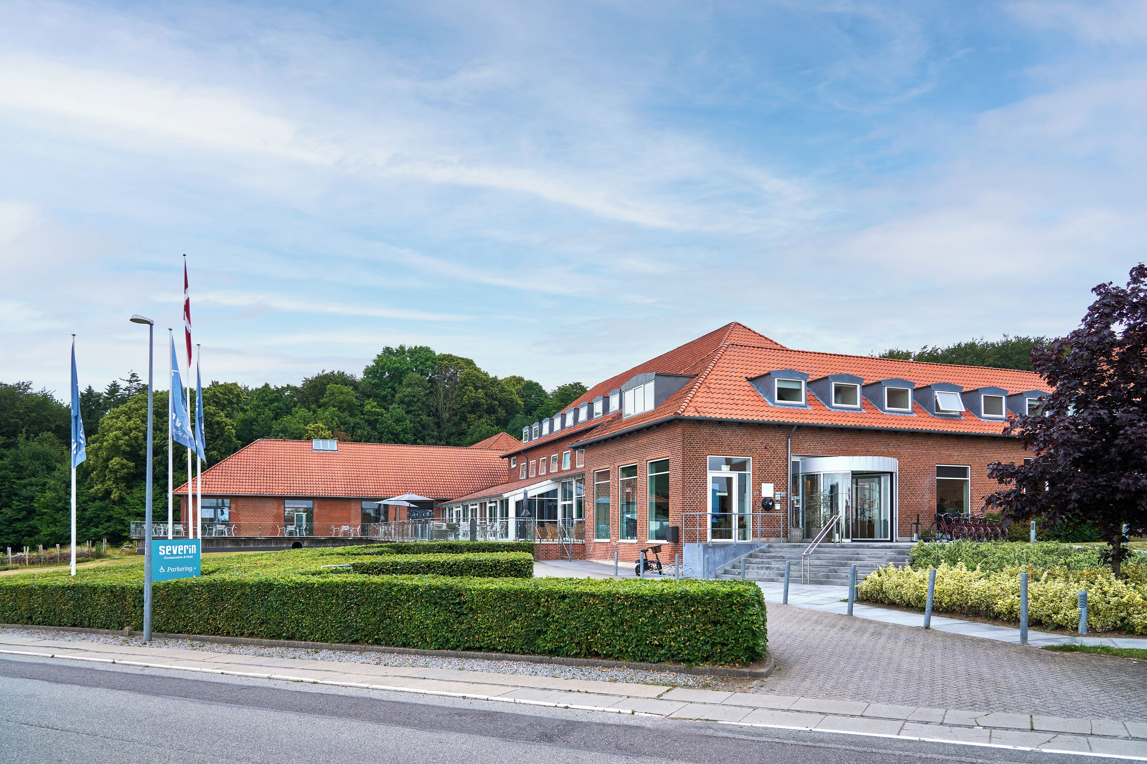 En rød murbygning med tegltag, en glasindgang og en belagt indkørsel.