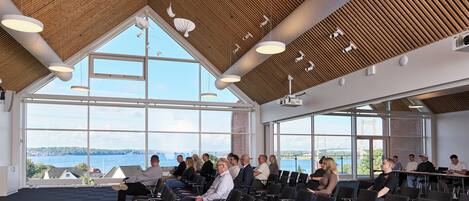 A conference room with a high ceiling, large windows, and a view of a bridge and water.