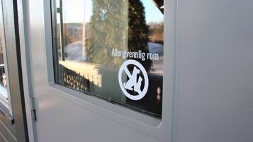 A window with a sticker indicating an allergy-friendly room and a reflection of a tree and a building.